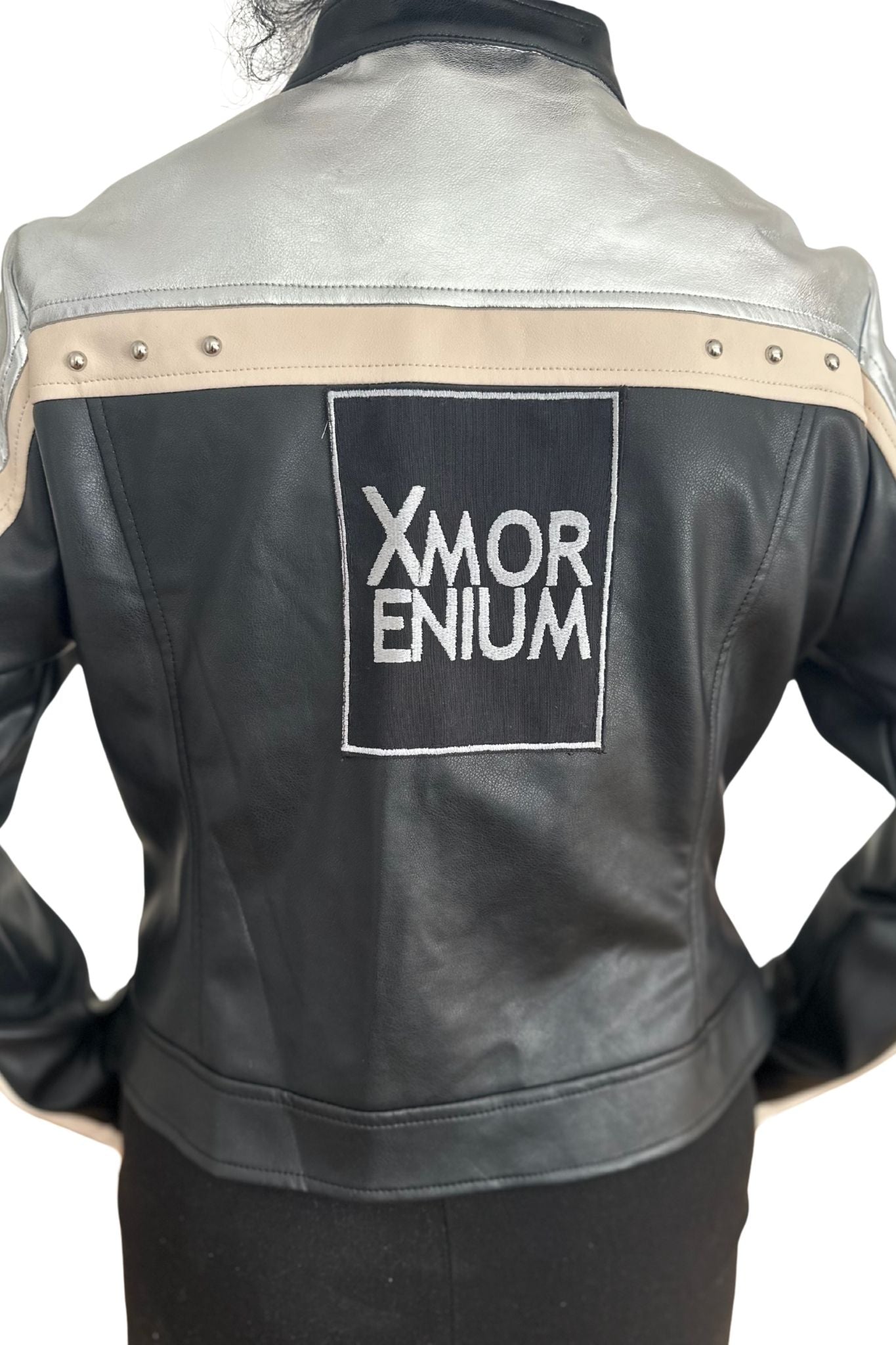 Person trägt silber-schwarze Kunstlederjacke mit großem Xmorenium-Logo auf dem Rücken und beiger Zierleiste mit Nieten.