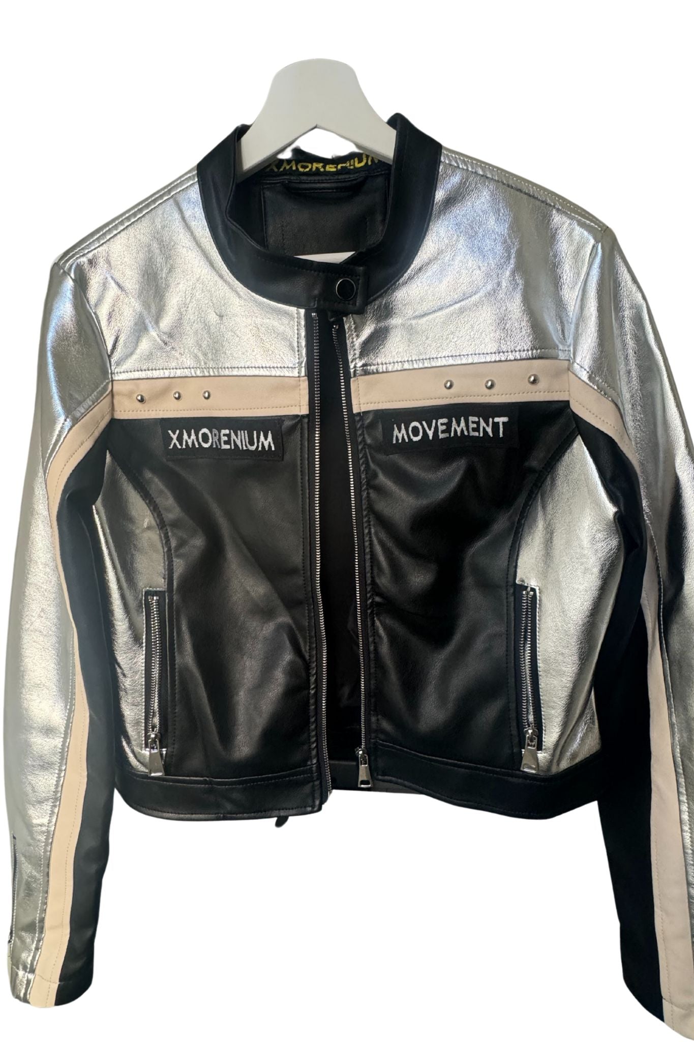 Silber-schwarze Kunstlederjacke mit Xmorenium- und Movement-Patches auf Bügel, beige Akzente und Reißverschlüsse sichtbar.