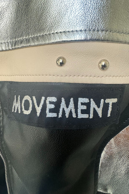 Detailaufnahme des Movement-Schriftzugs auf der silber-schwarzen Kunstlederjacke mit beiger Ziernaht und Nieten.