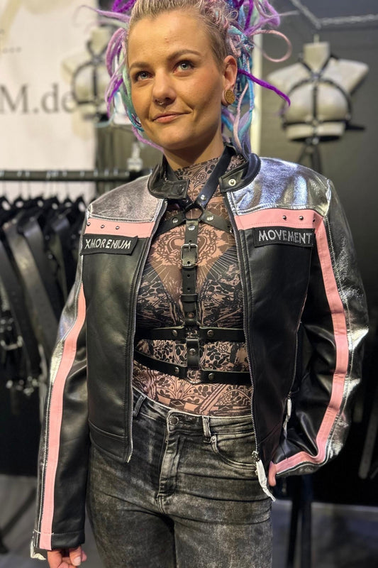 Frau trägt silber-schwarze Kunstlederjacke mit rosa Details und Harness von Xmorenium auf einer Messe für Fetischmode.